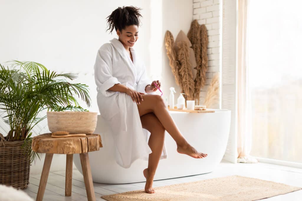 Woman sitting on bath tub while preparing to shave her legs.